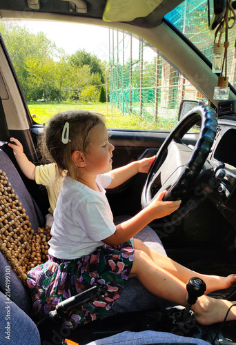 Young girl sitting at the steering wheel of a car with her little brother