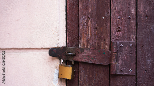 Old brown wooden door locked with a metal padlock on a rusty latch. Concept of safety, security, privacy, and access control. Rustic architectural background.