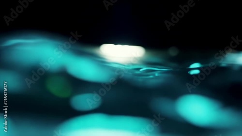 Rippling water surface illuminated by soft light creates a tranquil scene with reflections and gentle waves in a dark environment, showcasing fluid motion and depth