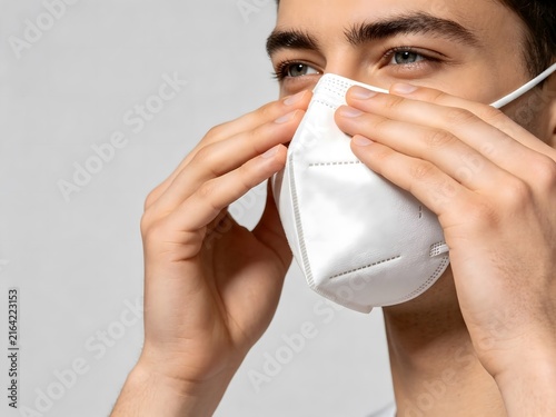 Young man adjusting white protective face mask for safety