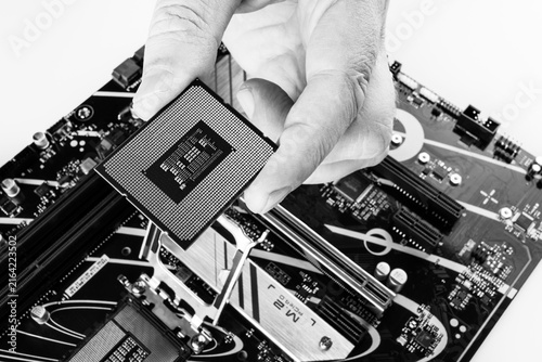 Close-up of a man holding a brand-new computer processor in his hand, with a motherboard visible in the background, black and white photo
