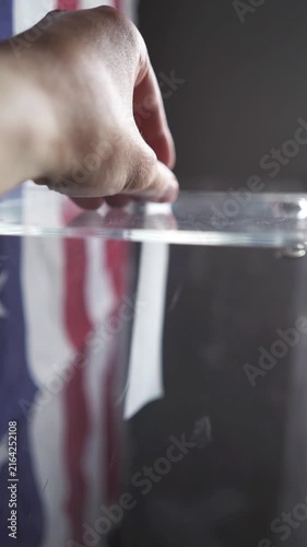 POV of voter inserting ballot sheet into slot of transparent box at US polling place