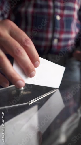 Voter walking up and inserting ballot into slot of transparent box, front view