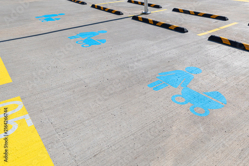 Designated family parking lot spots marked with blue painted symbols of a mother with baby stroller on sunny concrete pavement with yellow lane markings and wheel stops.