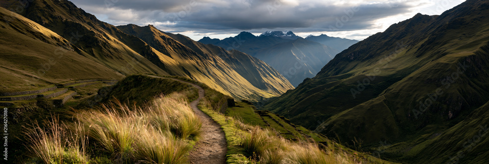 Naklejka premium impressive historic inca road winding through the andes, ancient stone path across dramatic mountain terrain, remote inca trail surrounded by terraces and snowcapped peaks