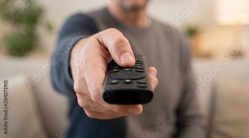 Person holding TV remote control toward camera, symbolizing entertainment, technology, home lifestyle, streaming, and digital convenience.