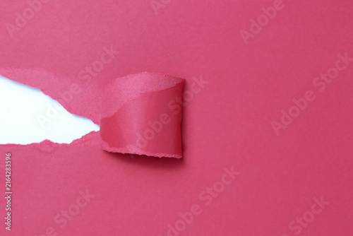 A close-up of torn pink paper revealing a white background