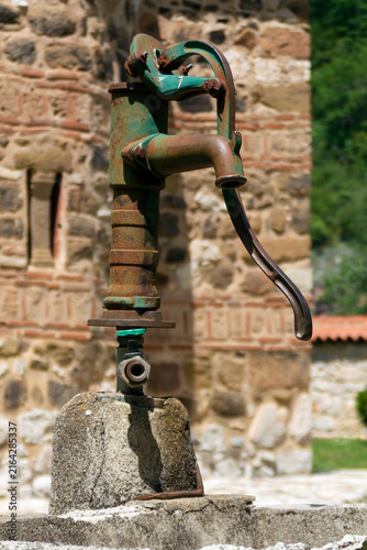 Old rusty damaged hand operated water pump in the monastery courtyard. Real photo. Adobe RGB color profile.