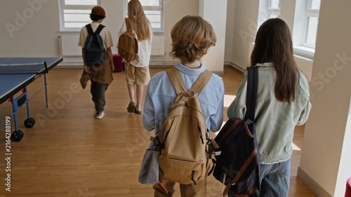Teenagers with backpacks walking down school hallway, rear view. Footage is ideal for educational marketing campaigns, school enrollment promos, and youth lifestyle ads