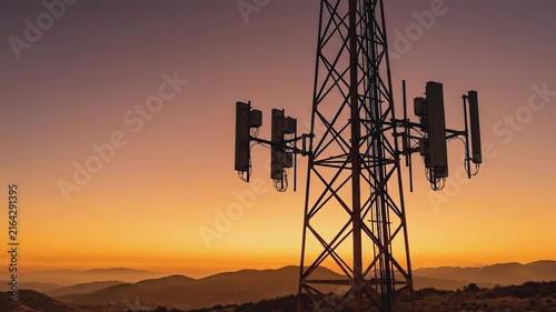 Telecommunication tower standing against warm golden sunset sky over mountain landscape