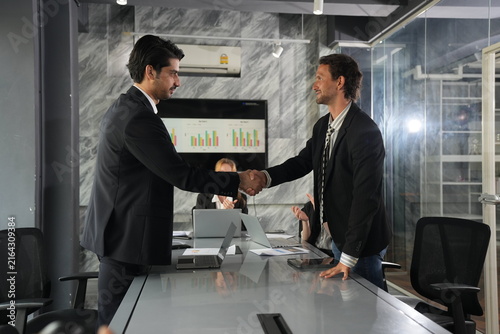 Foto Renewed pump of the handshake with laughter passing between the two colleagues, celebratory spirit glowing against the boardroom graph display in a bright modern coworking office