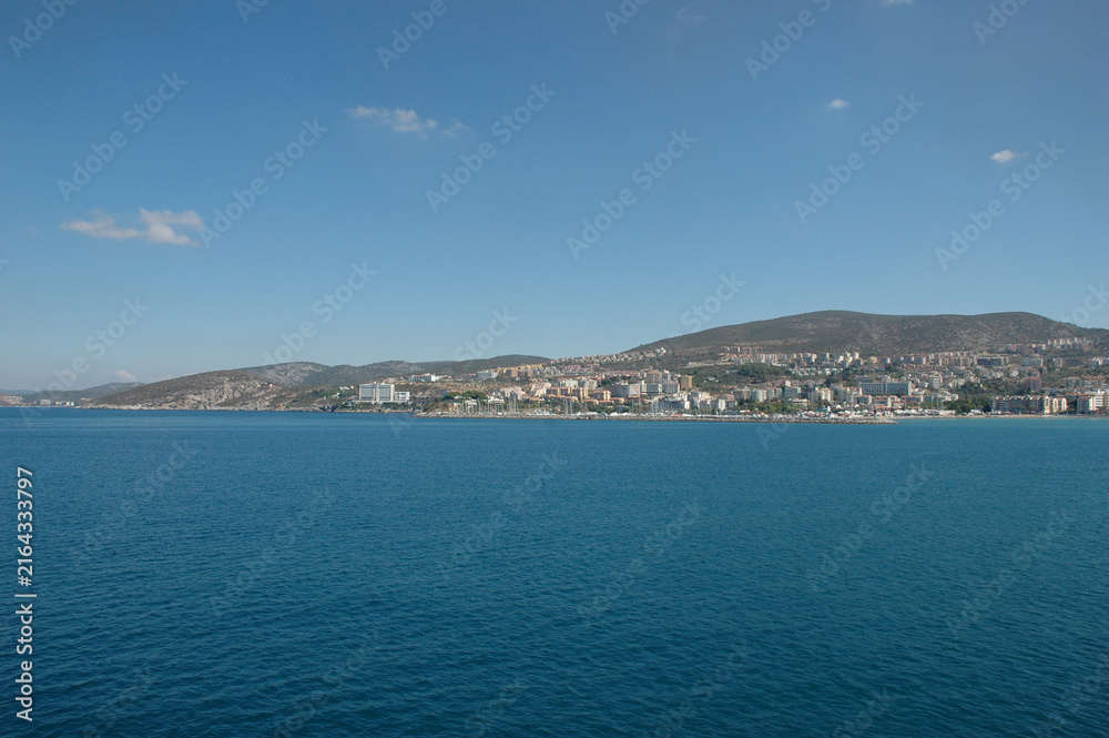 Fototapeta premium A scenic coastal view of the resort town Kusadasi with hotels and buildings on hillsides as seen from the calm blue waters of the Aegean Sea.