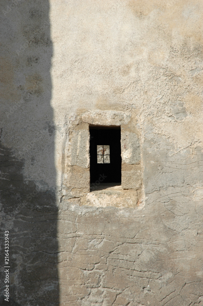 Naklejka premium Close up view of a small rectangular window slot with stone frame on the weathered exterior wall of the historic Church of Panagia Myrtidiotissa on Kythira island