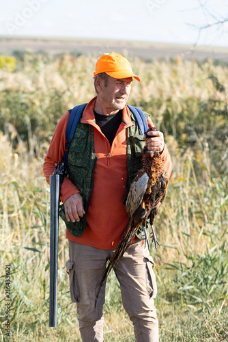 A hunter holds a pheasant in his hands. A successful hunt, a trophy game.