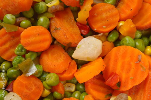 A detailed close up shot of a colorful vegetable mix featuring sliced crinkle cut carrots green peas corn and pearl onions