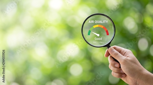 Hand holding magnifying glass over air quality meter showing good levels