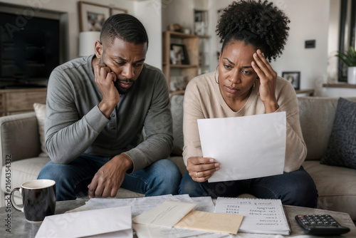 Black woman and her sad husband reading a bank document in a modern living room. Feelings of frustration and regret, bankruptcy, large debts to the bank. Bad news
