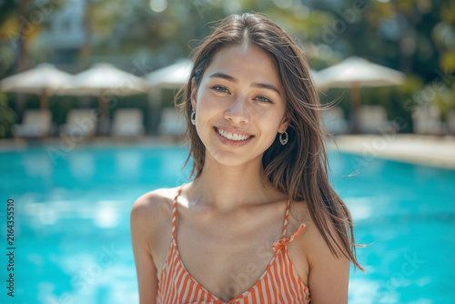 Portrait of happy beautiful young Asian woman smiles at camera by sunny outdoor swimming pool. Happy Asian lady on tropical resort vacation