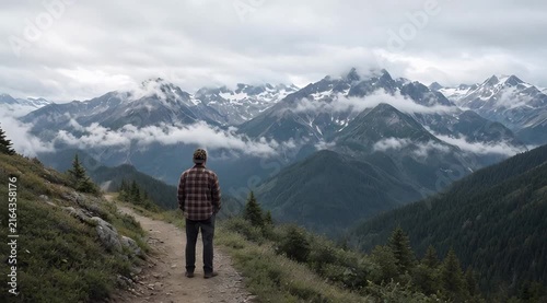 Solitary Hiker Standing on Trail Overlooking Majestic Mountains Shrouded in Clouds