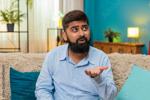 Foto Indian man at home rolls eyes showing ironic reaction during smartphone chat dismissing odd comment