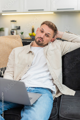 Obraz na płótnie Young man at home works on laptop feels tired and demotivated and takes deep sigh during hard task