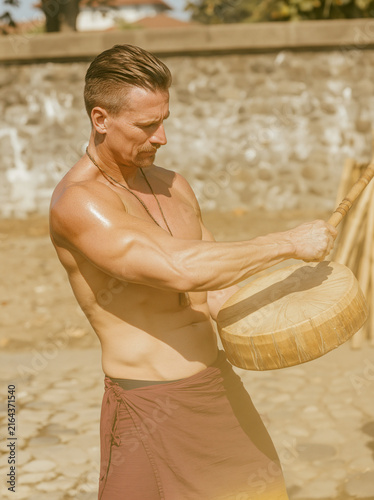 Man Holding Wooden Drum in Sunlit Courtyard