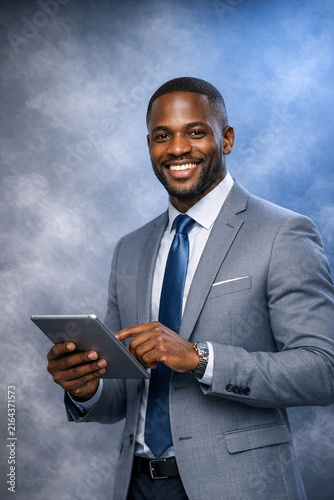 A smiling businessman in suit holding a tablet, representing professionalism and modern technology use.