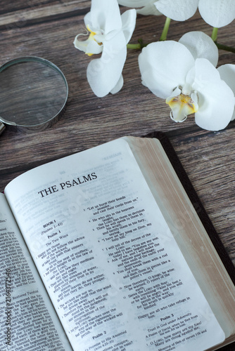 Psalms holy bible book on a wooden table with flowers and magnifying glass. Scripture study and reading concept.