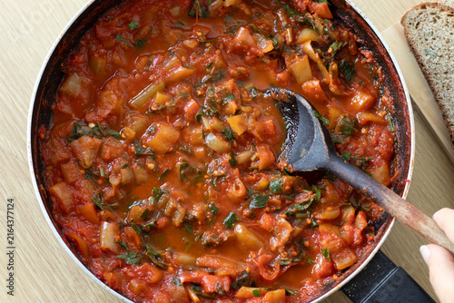 Cooking tomato pepper sauce in a pan with wooden spoon. Top view.