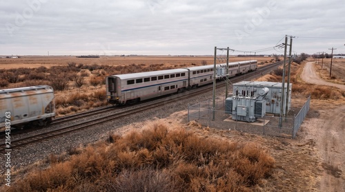 Train passes a gray electrical substation alongside a rural railway track
