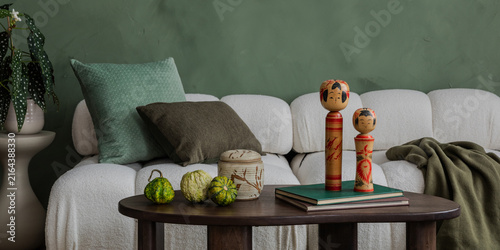 Modern living room interior with white sofa, green pillows, wooden coffee table, decorative dolls, plant, and earthy tones for cozy home design