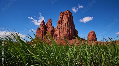 Towering Red Rock Formations Against a Clear Blue Sky with Lush Green Grasses in the Foreground