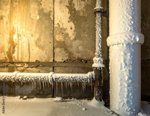 Frozen outdoor plumbing pipes covered with snow and ice beside a building