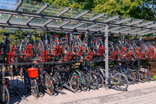Two tier bicycle parking rack filled with bikes under glass shelter, sustainable urban transport and cycling infrastructure concept