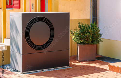Modern dark air source heat pump outdoor unit installed outside residential house, renewable heating system and green energy concept