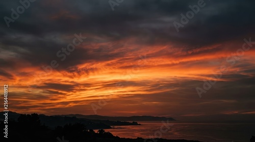 Dramatic fiery sunset over ocean waves with dark stormy sky above