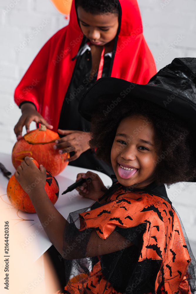 Fototapeta premium Costumed siblings joyfully carving pumpkins during Halloween festivities