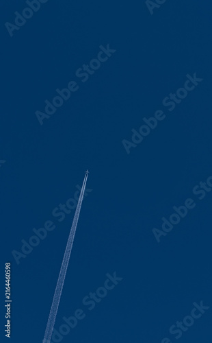 Airplane flying high in deep blue sky leaving long white condensation trail
