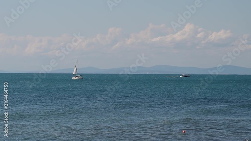 white sailboat cruises leisurely on the left, while a small motorboat speeds across the water on the right, leaving a visible wake.
