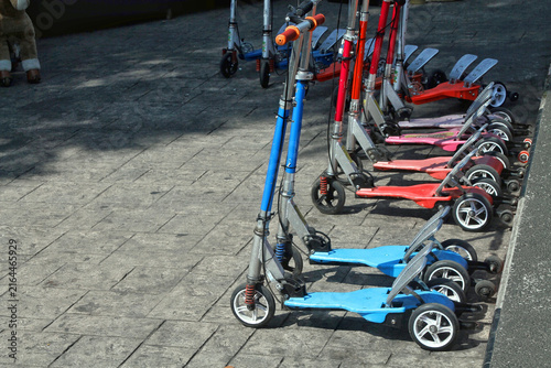 Row of Colorful Children's Kick Scooters Parked on Stone Pavement in Sunlight