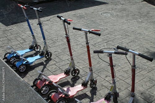Row of Colorful Children's Kick Scooters Parked on Stone Pavement in Sunlight