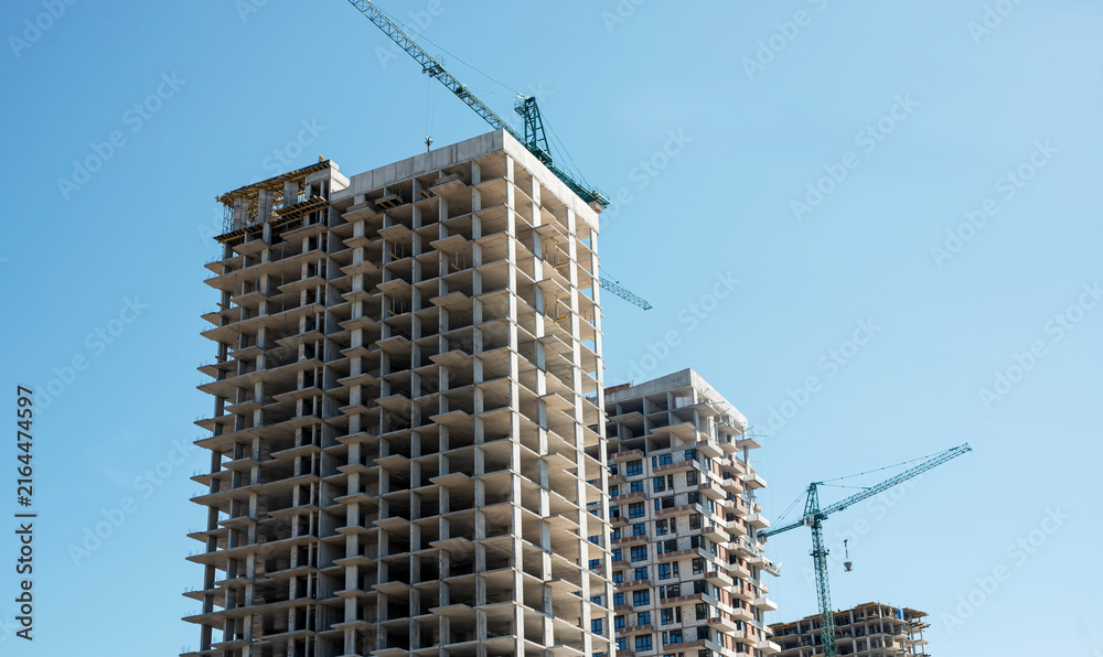 Fototapeta premium Modern residential buildings under construction with tower cranes and blue sky with white clouds