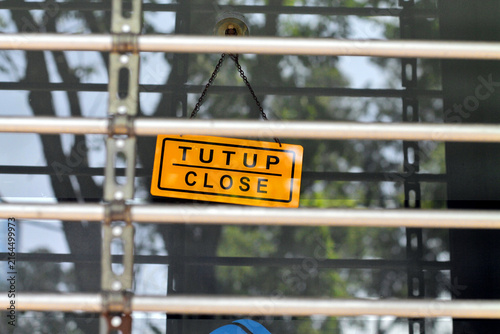 Yellow Close Sign Hanging Behind Metal Shutter on Closed Storefront