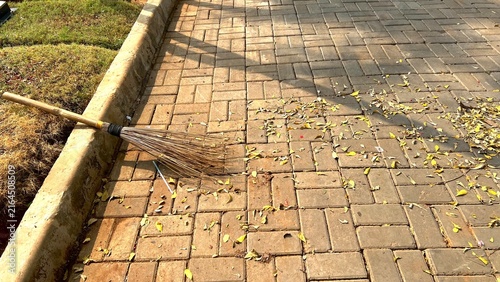 Konstfotografi A traditional outdoor broom lying on a paved brick walkway while scattered yellow leaves are being swept