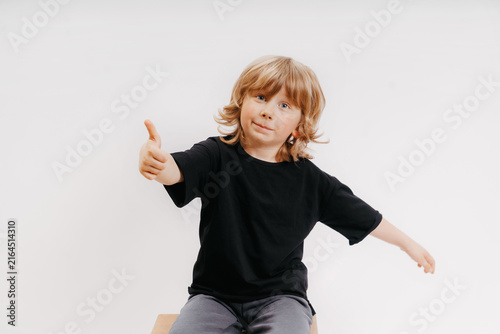 cute little blonde boy in black t-shirt is giving thumb up and smiling