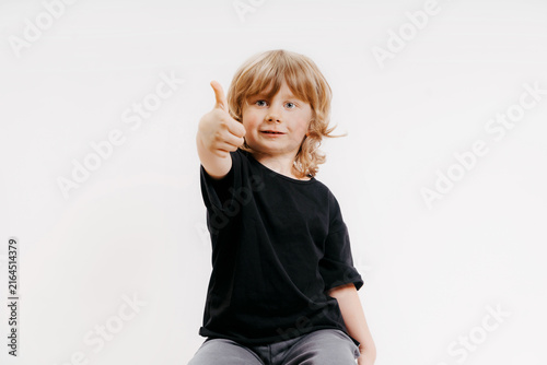 cute little blonde boy in black t-shirt is giving thumb up and smiling