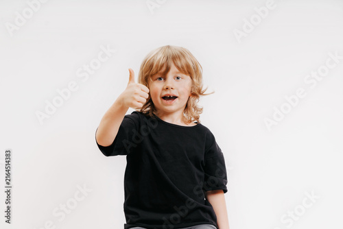 cute little blonde boy in black t-shirt is giving thumb up and smiling