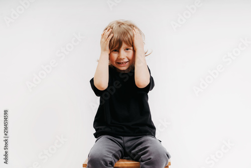 cute little blond boy in black T-shirt shows surprise and put his hand on his head