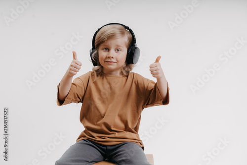 cute little boy in headphones and yellow T-shirt is giving the thumbs up gesture