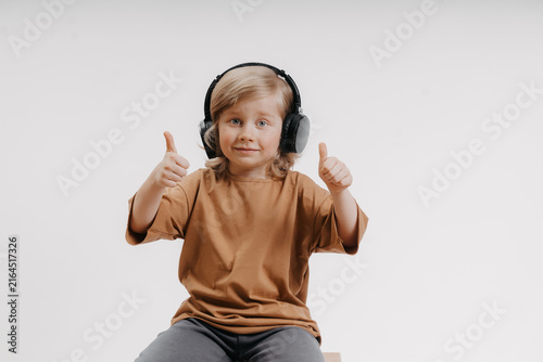 cute little boy in headphones and yellow T-shirt is giving the thumbs up gesture